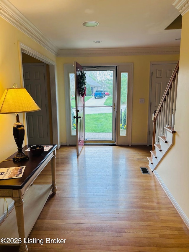 entryway with light wood-type flooring, baseboards, visible vents, stairs, and crown molding