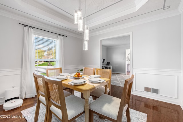 dining space featuring a raised ceiling, wood finished floors, ornamental molding, and visible vents