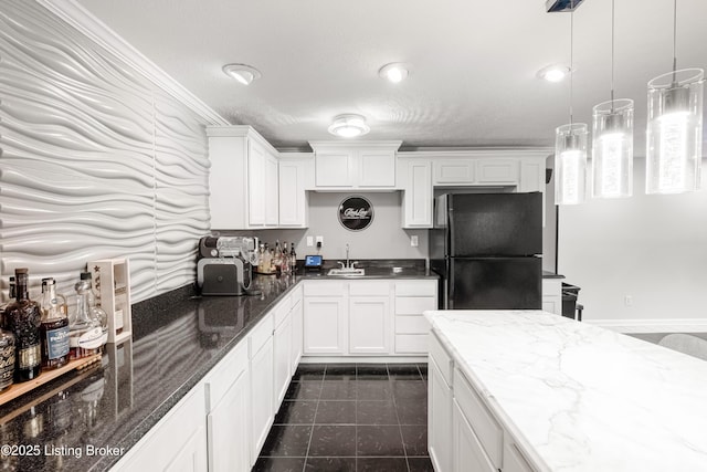 kitchen featuring dark stone countertops, a sink, freestanding refrigerator, white cabinetry, and pendant lighting