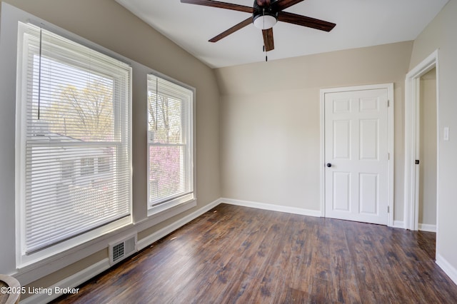 spare room with dark wood-style flooring, visible vents, baseboards, and a ceiling fan