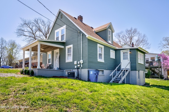 back of house featuring a porch, a chimney, central AC unit, and a lawn