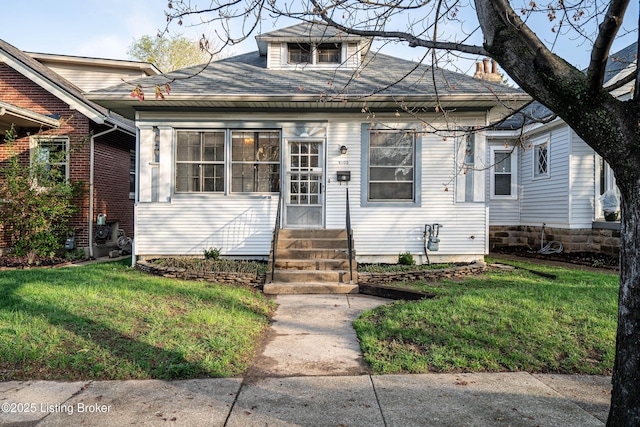 bungalow featuring entry steps, a front lawn, and a shingled roof