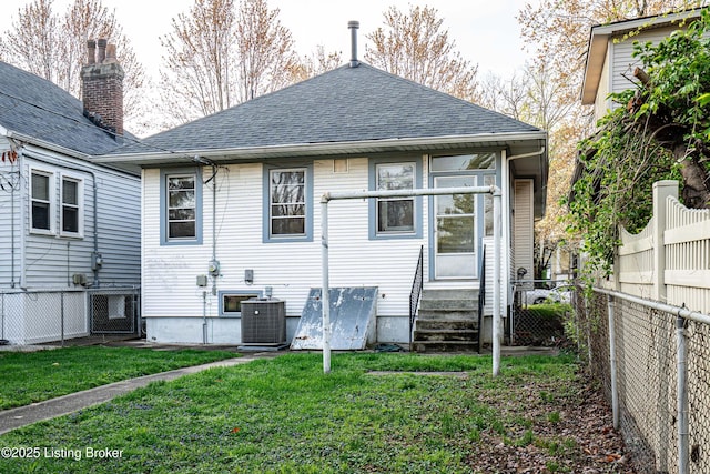 rear view of property featuring entry steps, a fenced backyard, a lawn, and roof with shingles