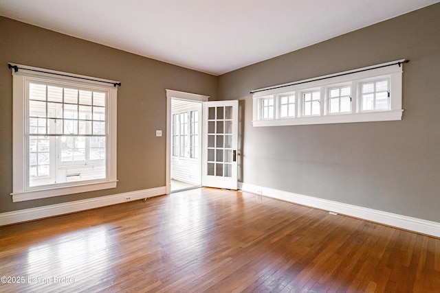 unfurnished room featuring a wealth of natural light, hardwood / wood-style flooring, and baseboards