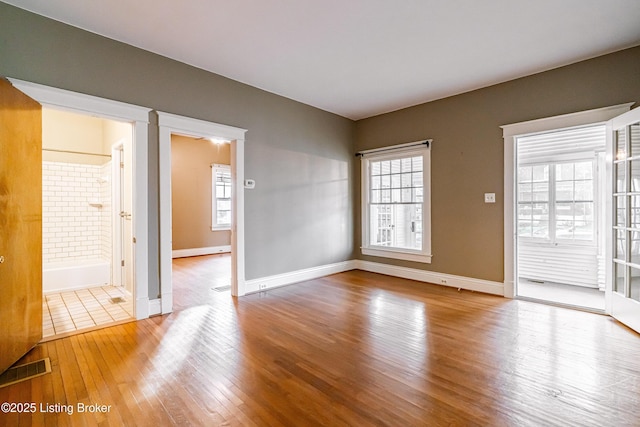 unfurnished room with wood-type flooring, visible vents, baseboards, and a healthy amount of sunlight