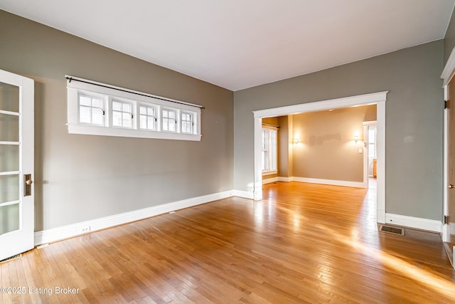 empty room featuring wood-type flooring, visible vents, and baseboards