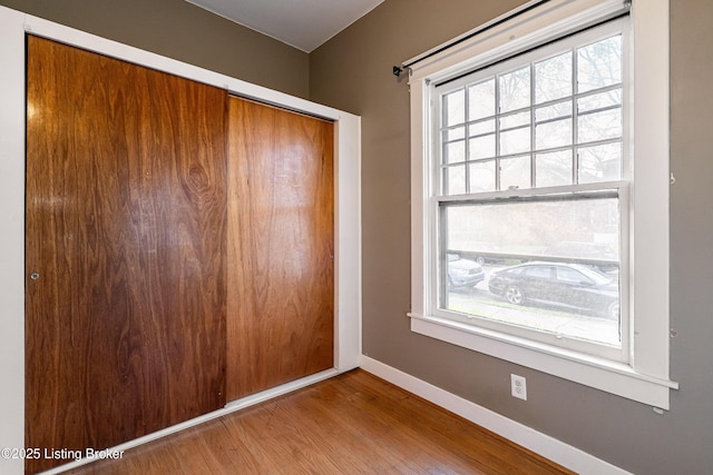 unfurnished bedroom featuring a closet, multiple windows, baseboards, and wood finished floors