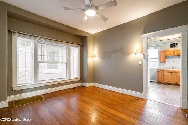 unfurnished room featuring ceiling fan, light wood-style flooring, visible vents, a sink, and baseboards