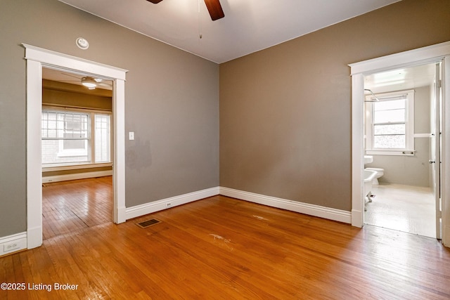 spare room featuring hardwood / wood-style floors, visible vents, baseboards, and a ceiling fan