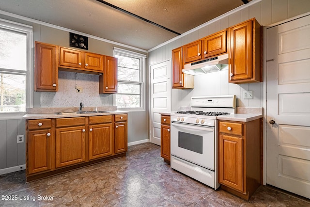 kitchen with a sink, light countertops, gas range gas stove, under cabinet range hood, and brown cabinetry