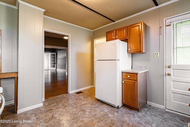 kitchen featuring ornamental molding, light countertops, freestanding refrigerator, visible vents, and brown cabinets