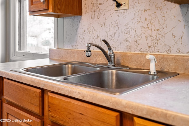 kitchen featuring brown cabinetry, wallpapered walls, a sink, and light countertops