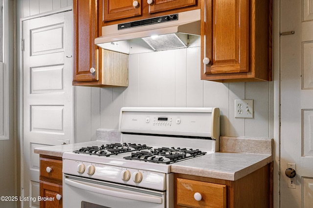kitchen featuring brown cabinets, light countertops, white gas range, and under cabinet range hood