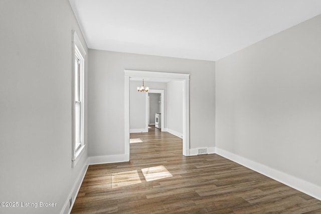 unfurnished room with a chandelier, wood finished floors, baseboards, and visible vents