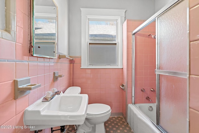 full bathroom with combined bath / shower with glass door, tile patterned flooring, toilet, tile walls, and a sink