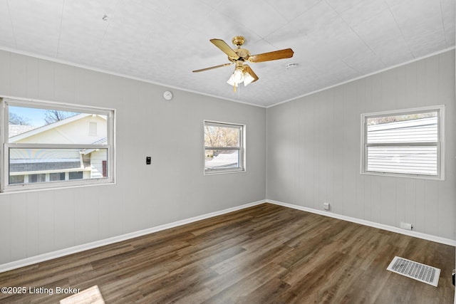 empty room featuring ornamental molding, a ceiling fan, visible vents, wood finished floors, and baseboards