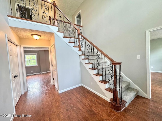 stairway with a textured ceiling, a high ceiling, baseboards, and wood finished floors