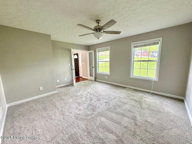 empty room with a textured ceiling, visible vents, ceiling fan, carpet flooring, and baseboards