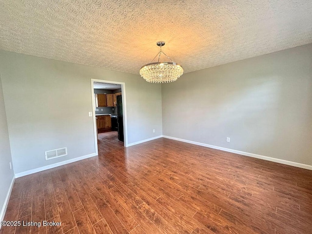 unfurnished room featuring baseboards, a notable chandelier, visible vents, and dark wood-style floors