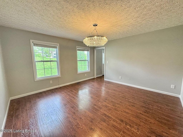 empty room featuring baseboards, dark wood finished floors, an inviting chandelier, and a textured ceiling