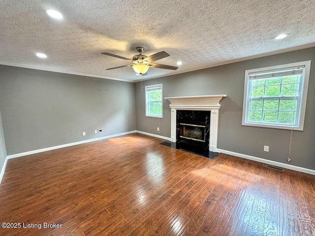 unfurnished living room with a high end fireplace, wood finished floors, ornamental molding, a textured ceiling, and baseboards