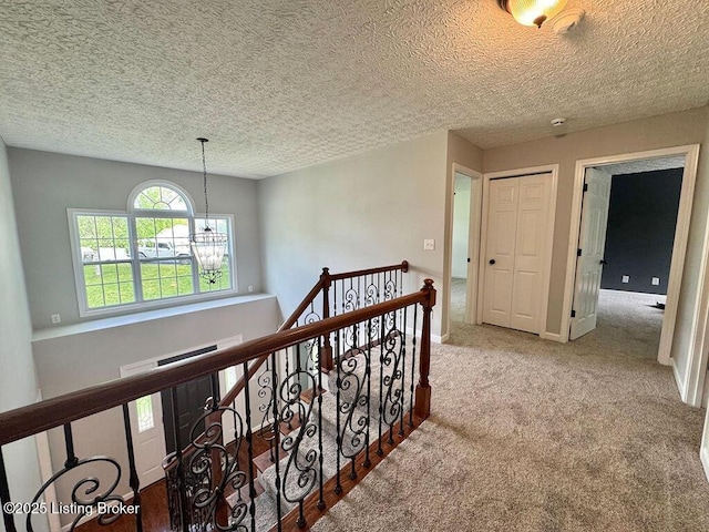 corridor featuring a chandelier, a textured ceiling, carpet flooring, and an upstairs landing