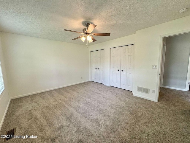 unfurnished bedroom with multiple closets, a textured ceiling, carpet, and visible vents