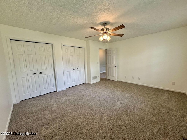 unfurnished bedroom featuring a textured ceiling, baseboards, visible vents, multiple closets, and carpet floors