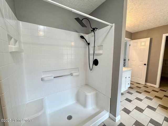 bathroom featuring walk in shower, vanity, a textured ceiling, tile patterned floors, and baseboards