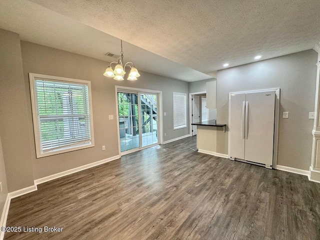 unfurnished living room with a textured ceiling, baseboards, an inviting chandelier, visible vents, and dark wood-type flooring