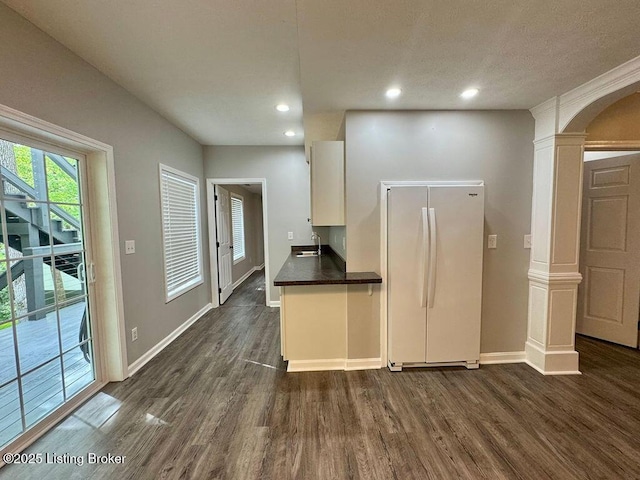 kitchen featuring a sink, freestanding refrigerator, dark countertops, decorative columns, and dark wood-style flooring