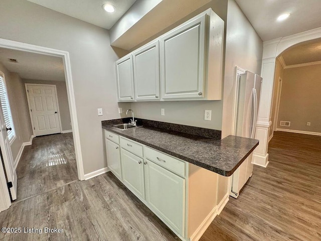 kitchen featuring wood finished floors, a sink, freestanding refrigerator, dark countertops, and baseboards