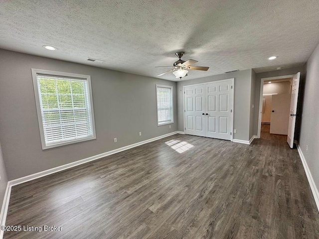 unfurnished bedroom featuring a textured ceiling, baseboards, dark wood-style floors, and visible vents