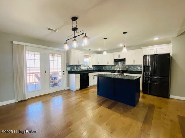 kitchen with visible vents, dark countertops, under cabinet range hood, black appliances, and decorative backsplash