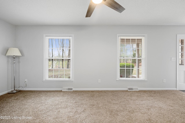 carpeted spare room with visible vents, ceiling fan, and baseboards