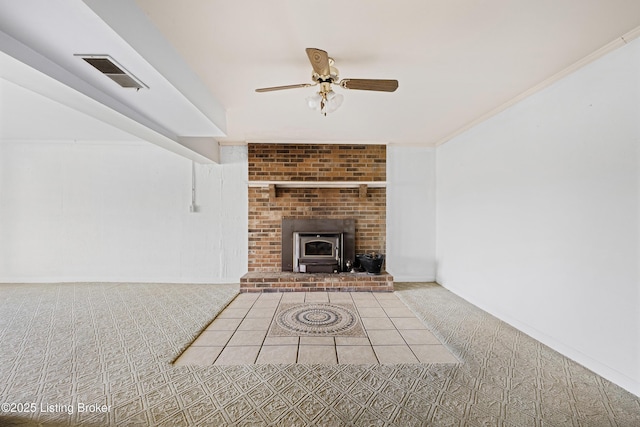 unfurnished living room featuring a wood stove, a ceiling fan, visible vents, and carpet floors