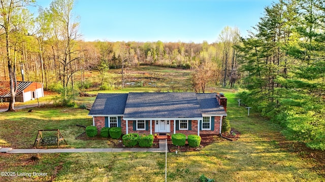 view of front of house with a view of trees, a chimney, a front yard, and brick siding