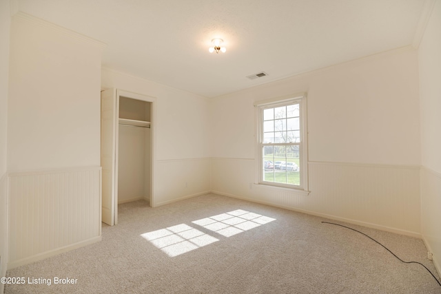 unfurnished bedroom featuring a closet, ornamental molding, visible vents, a wainscoted wall, and carpet flooring