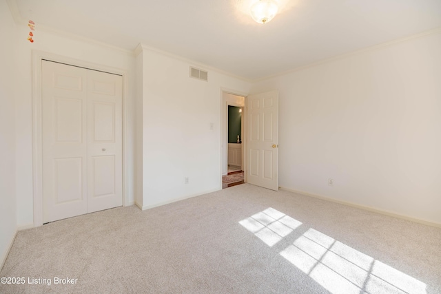 unfurnished bedroom with baseboards, a closet, ornamental molding, carpet floors, and visible vents