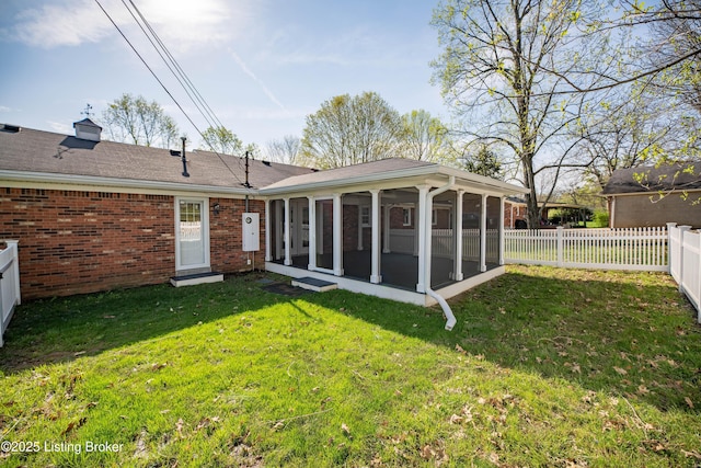 back of house featuring a yard, a fenced backyard, brick siding, and a sunroom