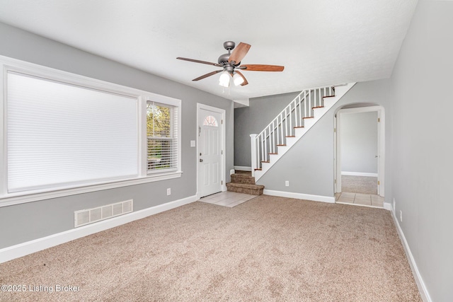 carpeted entrance foyer with visible vents, baseboards, arched walkways, a ceiling fan, and stairway