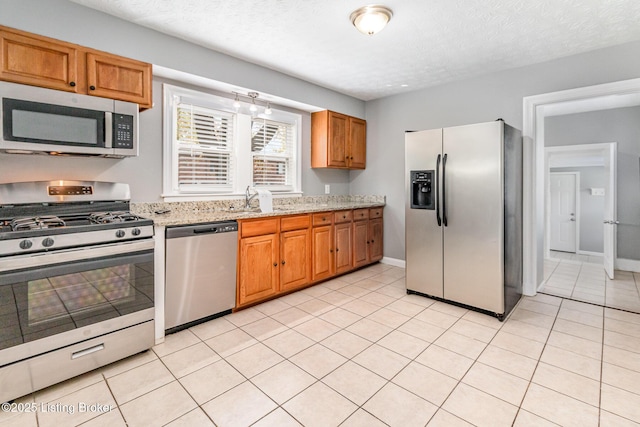 kitchen featuring light tile patterned floors, brown cabinets, light stone counters, and appliances with stainless steel finishes