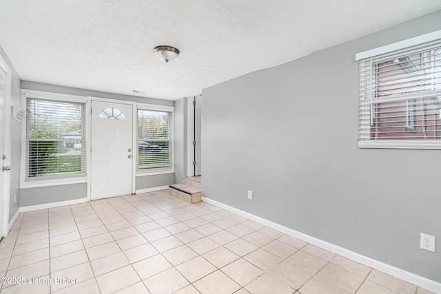 entryway with light tile patterned floors, baseboards, and a textured ceiling