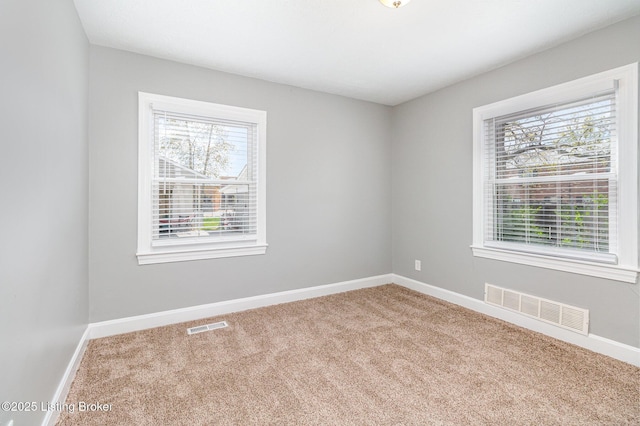 carpeted spare room with a healthy amount of sunlight, baseboards, and visible vents