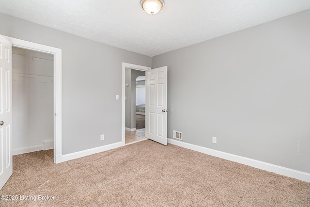 unfurnished bedroom featuring visible vents, baseboards, a closet, and light colored carpet