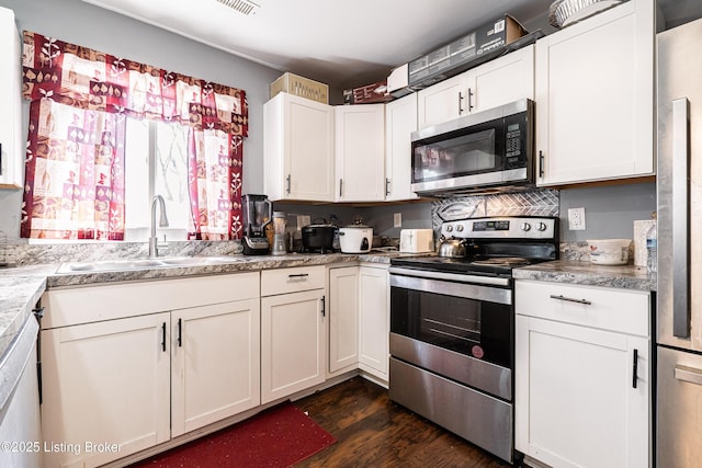 kitchen with appliances with stainless steel finishes, dark wood-style flooring, a sink, and white cabinetry