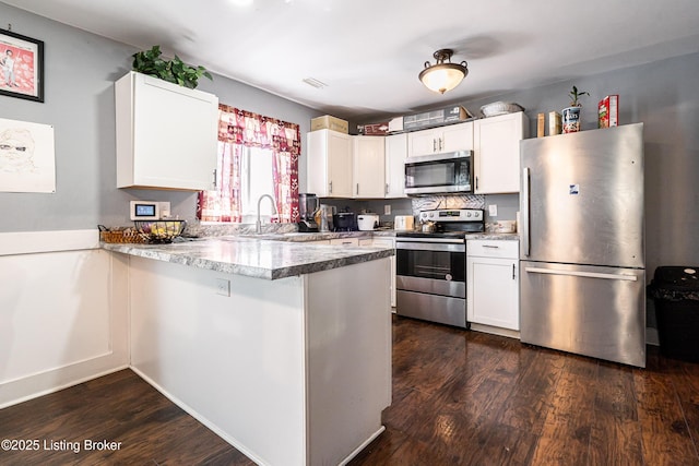kitchen with a peninsula, dark wood-style floors, white cabinets, appliances with stainless steel finishes, and a sink