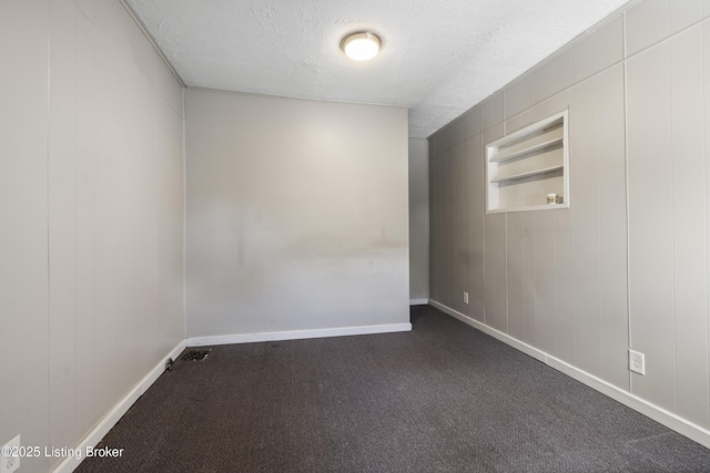 unfurnished room with dark carpet, baseboards, and a textured ceiling