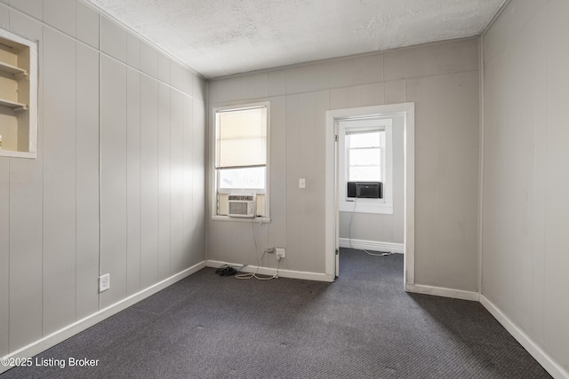 unfurnished room featuring baseboards, dark colored carpet, a textured ceiling, and cooling unit