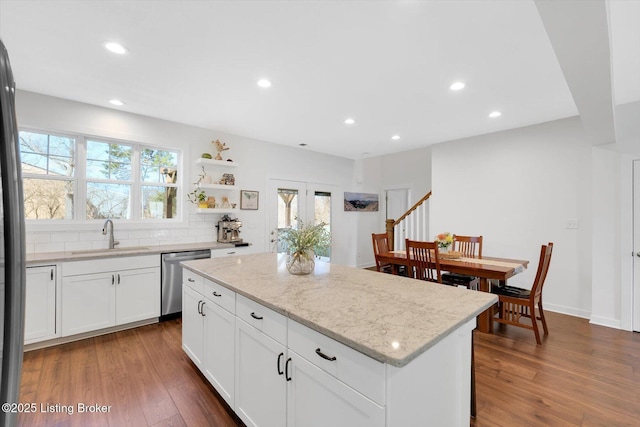 kitchen featuring stainless steel dishwasher, a kitchen island, wood finished floors, a sink, and decorative backsplash